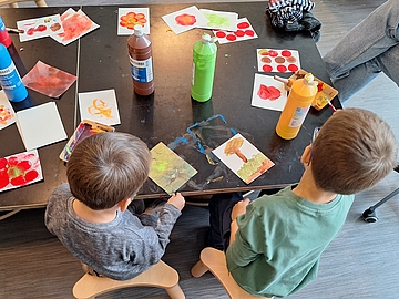 Kinder sitzen an einem Tisch mit Malsachen und angefangenen Bildern